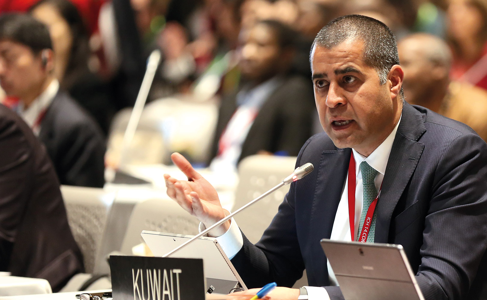 Ambassador Adam Al Mulla speaking into a small microphone at a conference. 