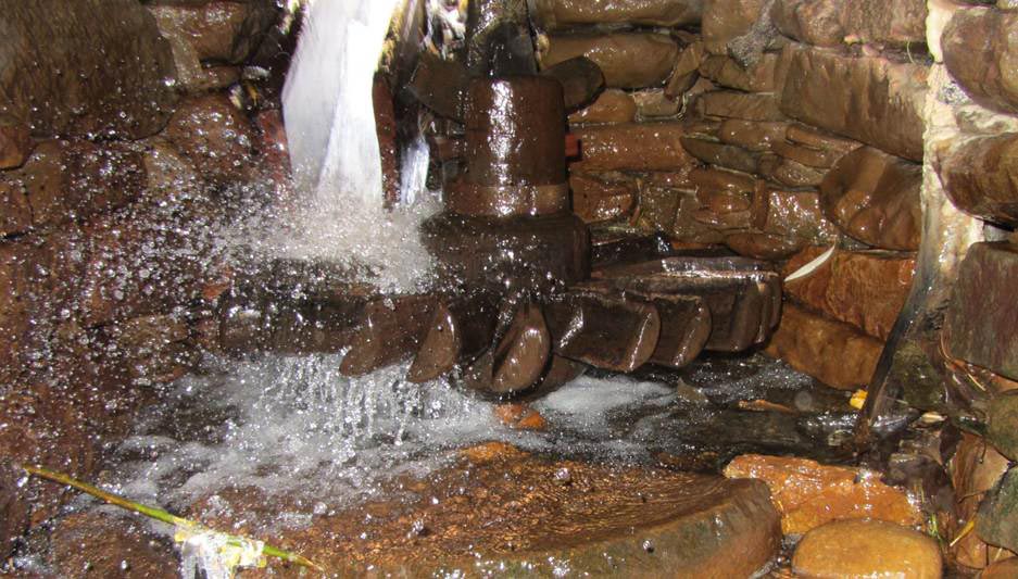 Stone waterwheel in a stream beneath a small waterfall.