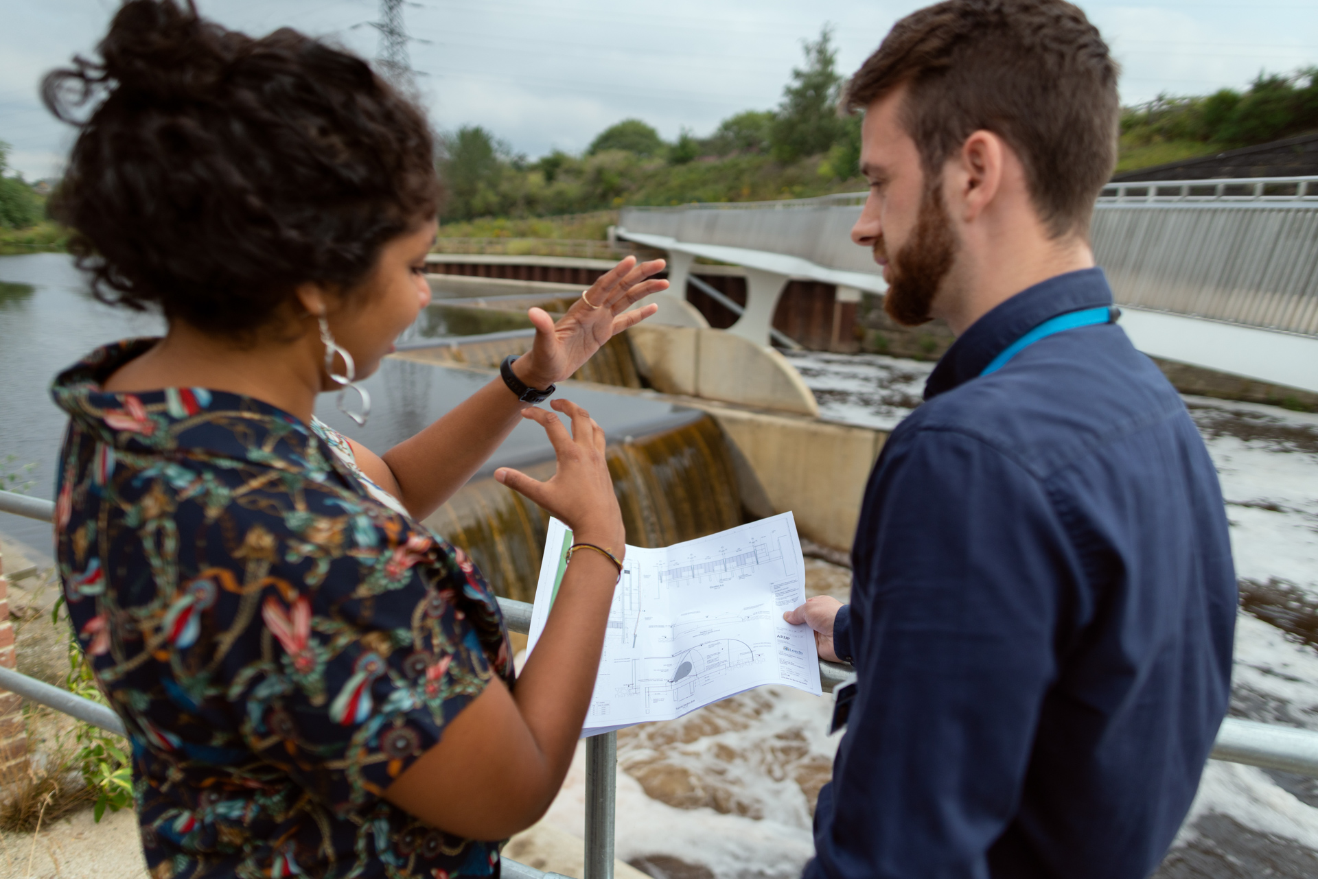 Two people holding a diagram at a dam. 