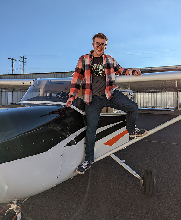 Andrew Dassonville sitting on the wing of a small airplane, smiling.