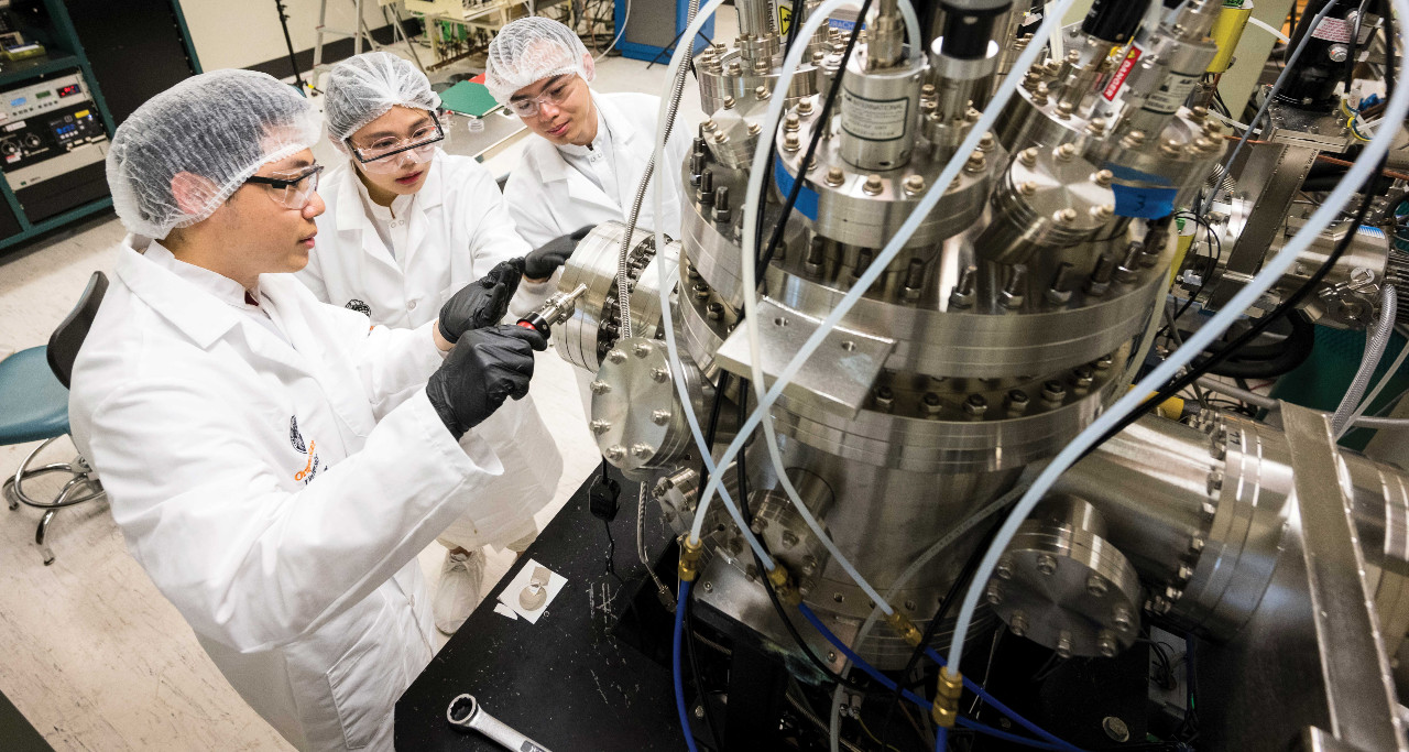 Three students in lab uniform working on a machine.
