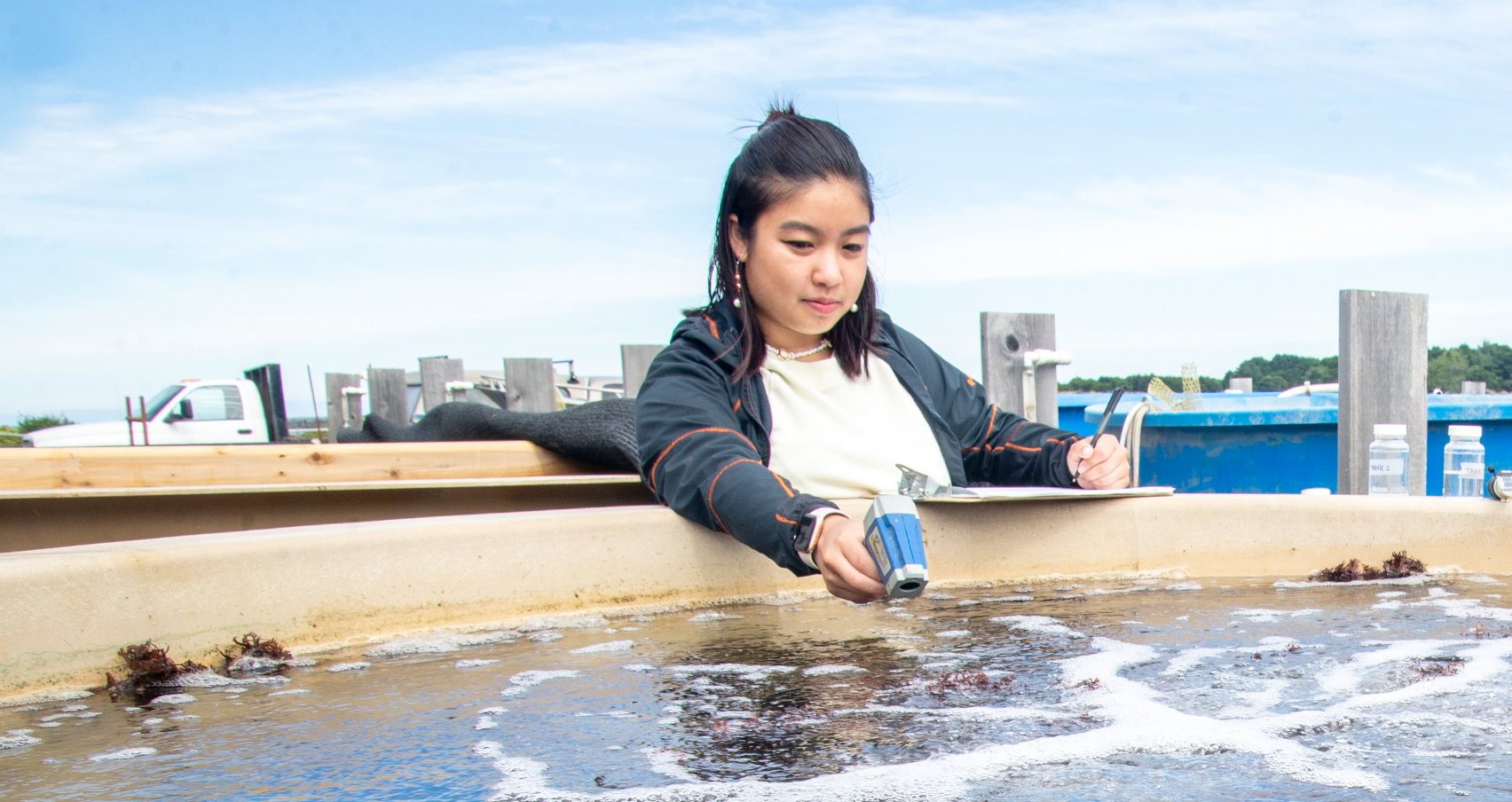 A student researcher testing water in a basin with a thermal reader.