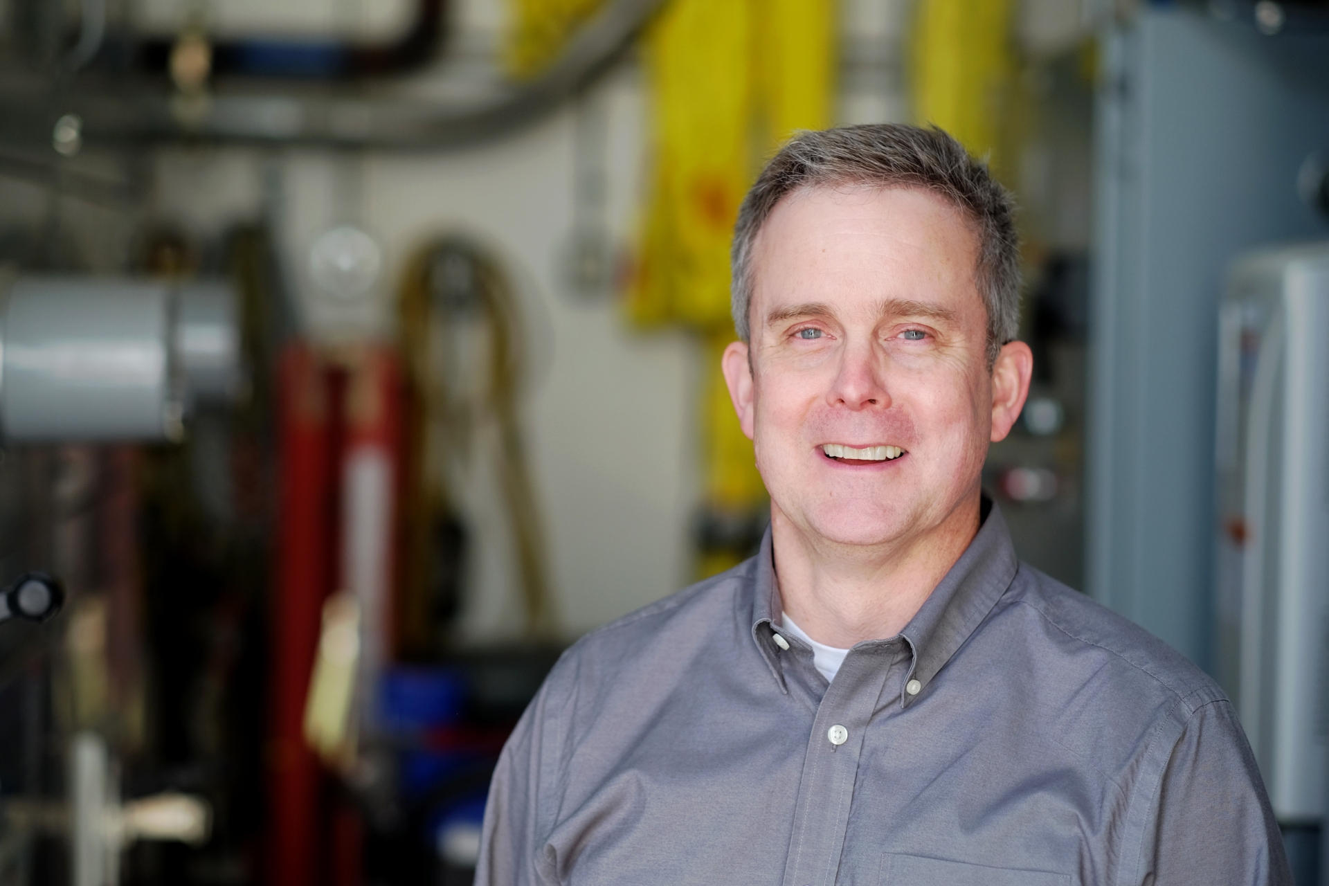 A portrait of a faculty member sitting in a nuclear engineering facility looking at the camera.