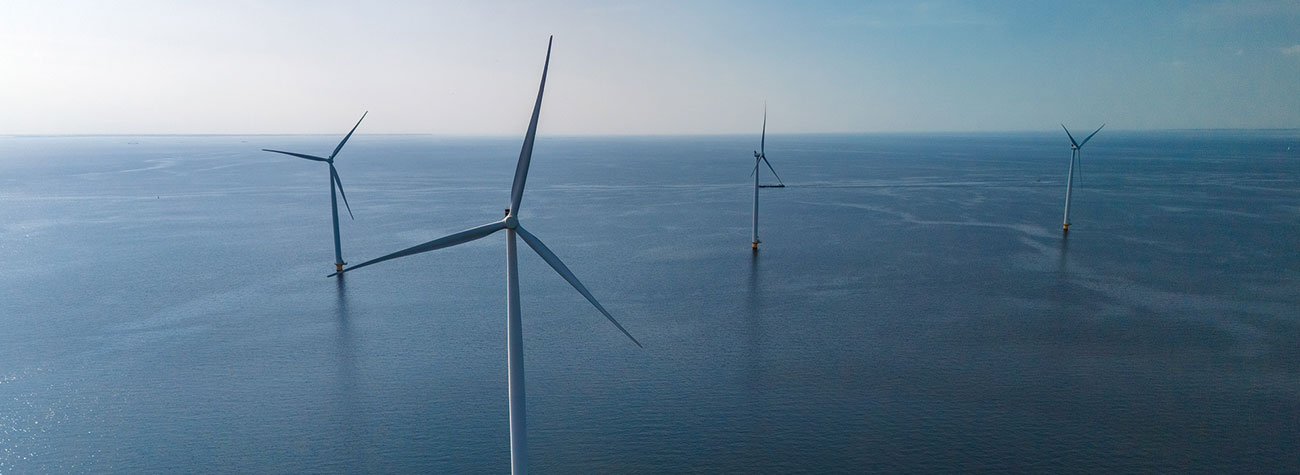 Four wind turbines in the ocean with the horizon in the distance. 