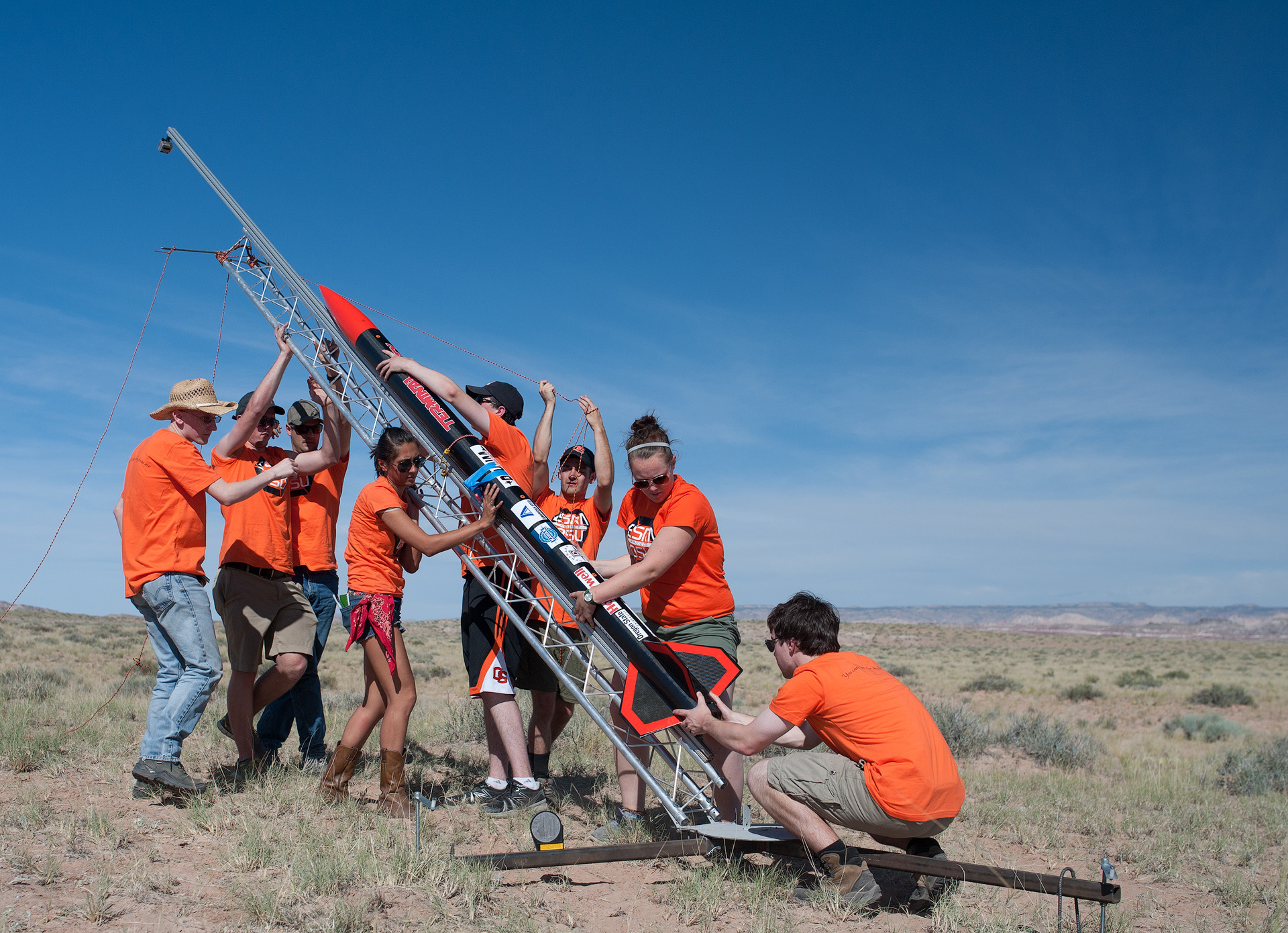 Aerospace engineering students in orange shirts, trying to launch a small rocket.