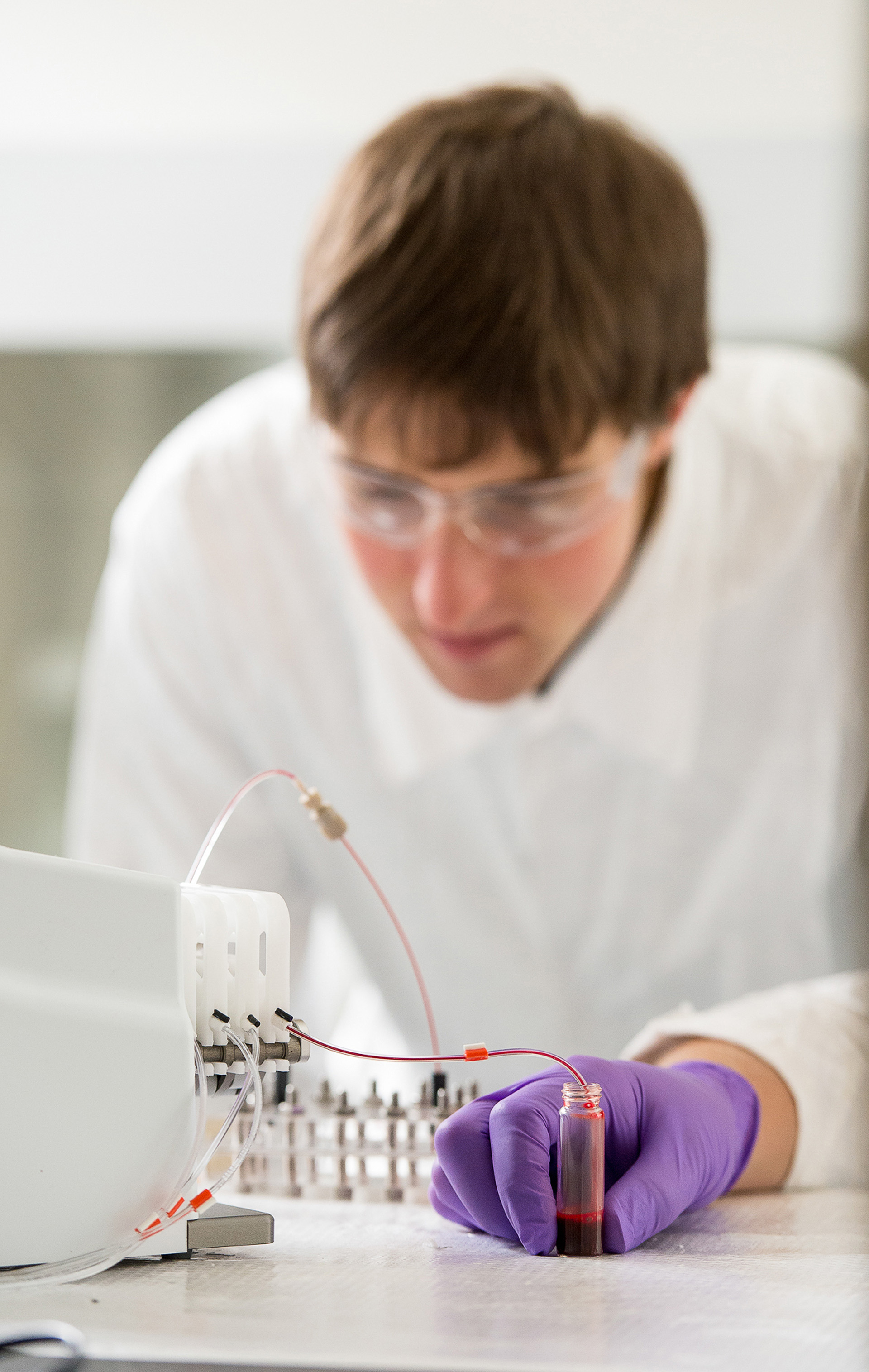 A bioengineer using a machine to test a red liquid in a vial.