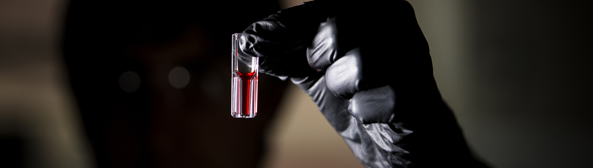 A lab technician holding up a test tube containing red liquid.