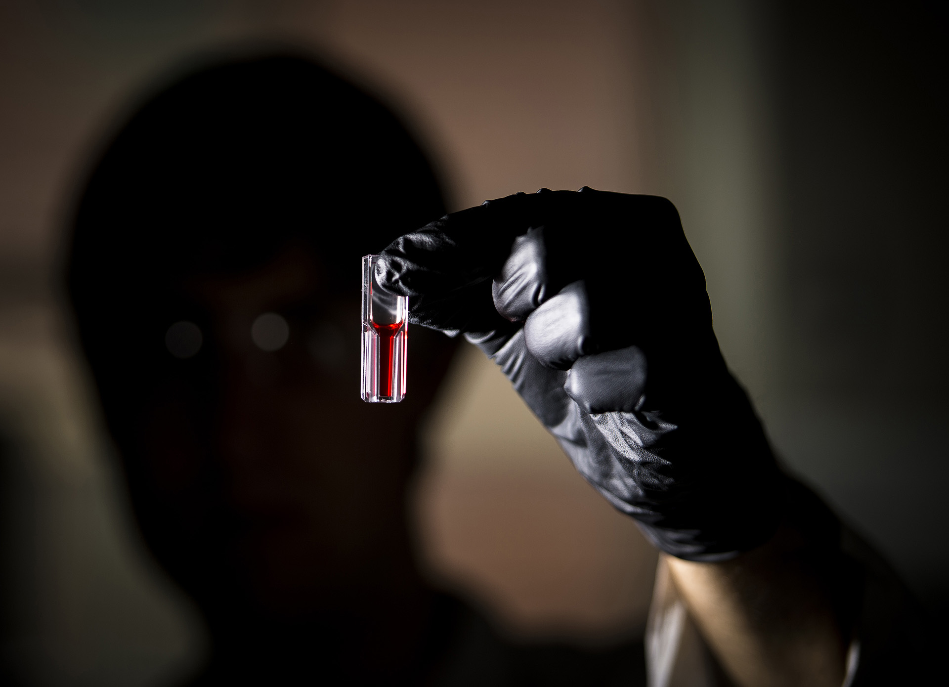 A lab technician holding up a test tube containing red liquid.