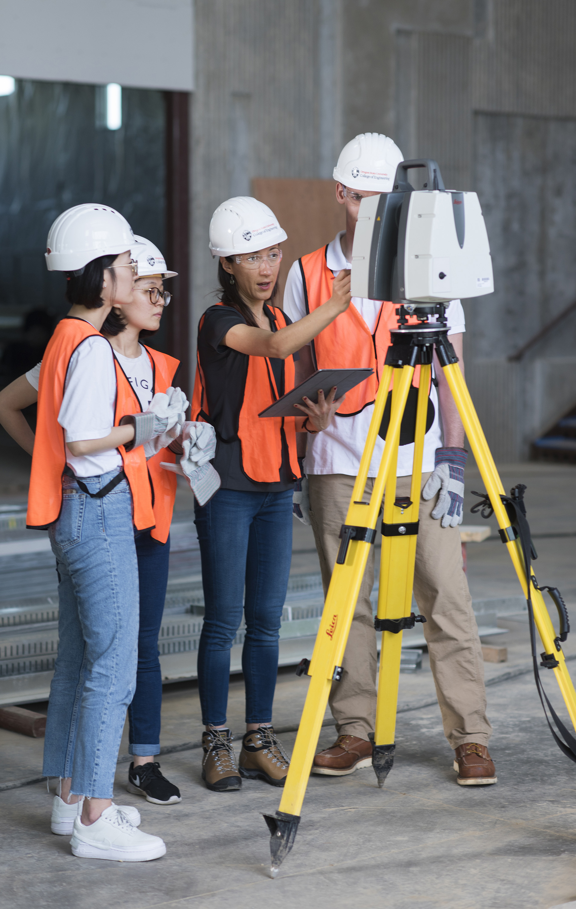 Professor Yelda Turkan and engineering students in orange safety vests looking through a surveyor camera.