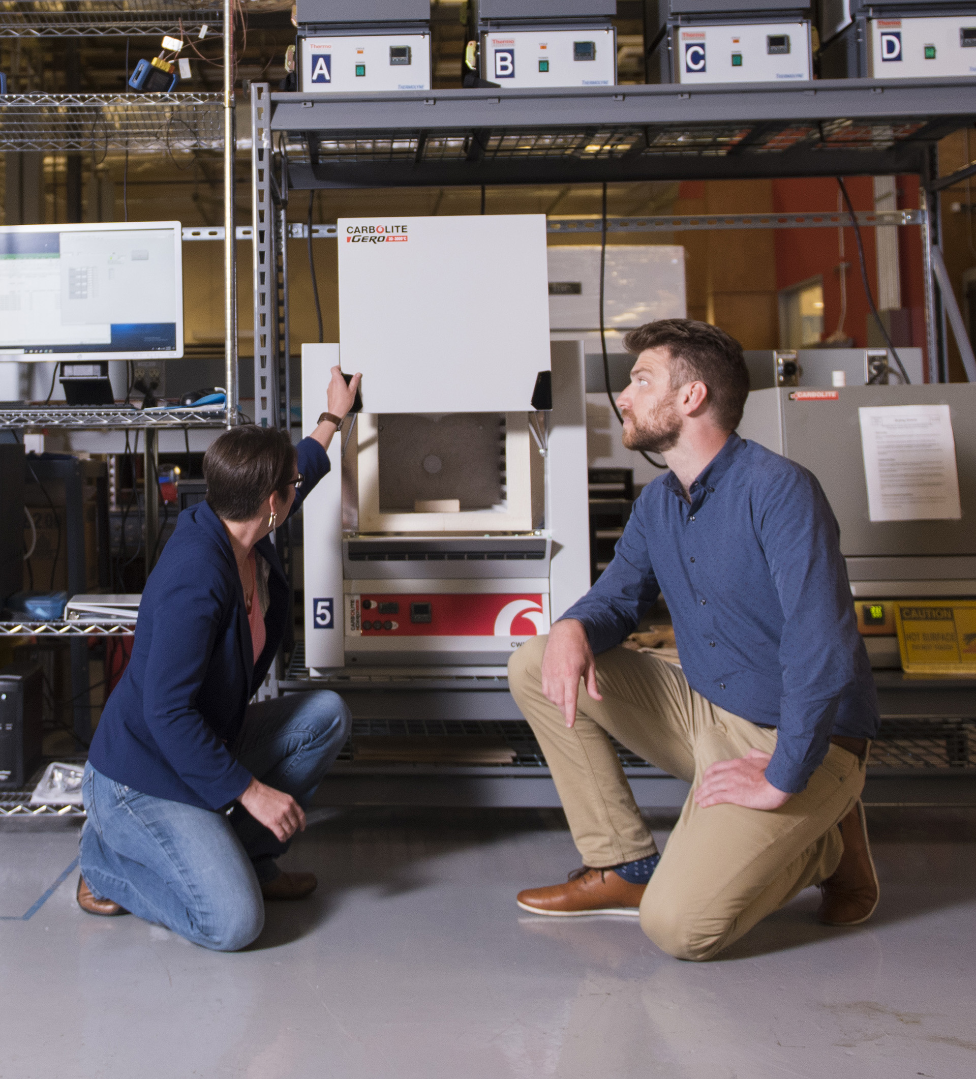 Industrial engineering Alumni Sam Briggs kneeling on the floor, working with a high temperature furnace.