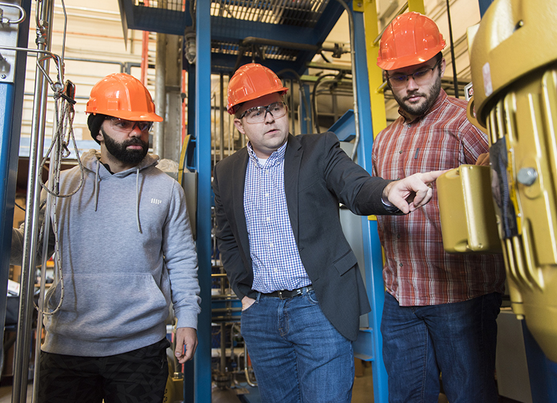 Three people in hard hats discussing a piece of equipment.