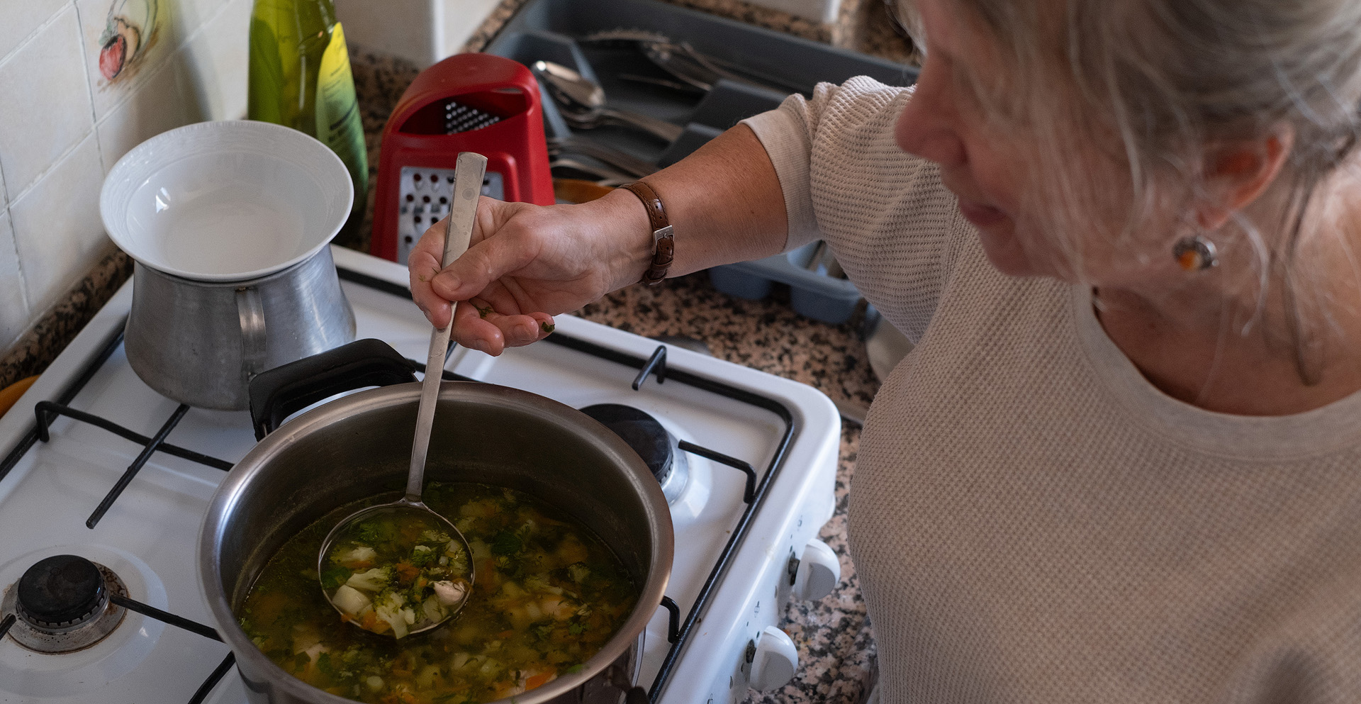 An elderly person cooking stew in a pot.