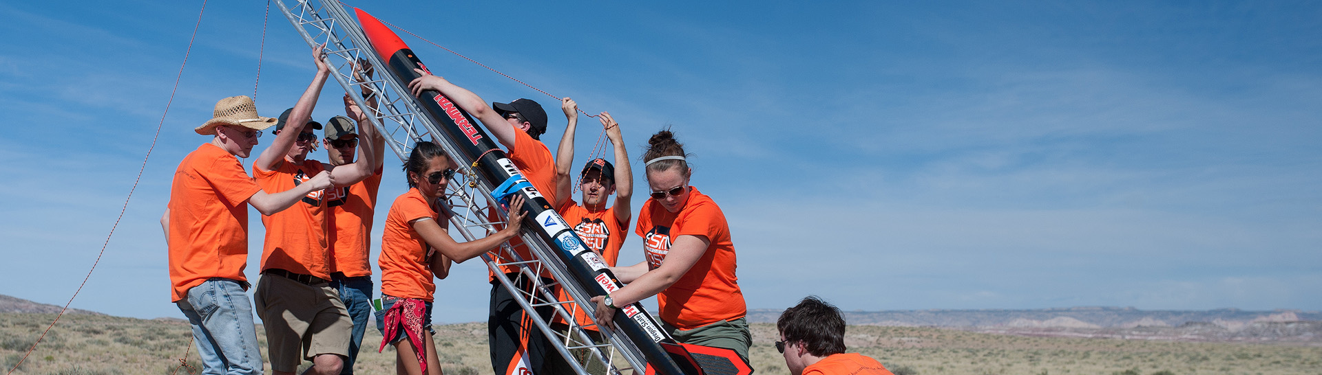 Aerospace engineering students in orange shirts, trying to launch a small rocket.