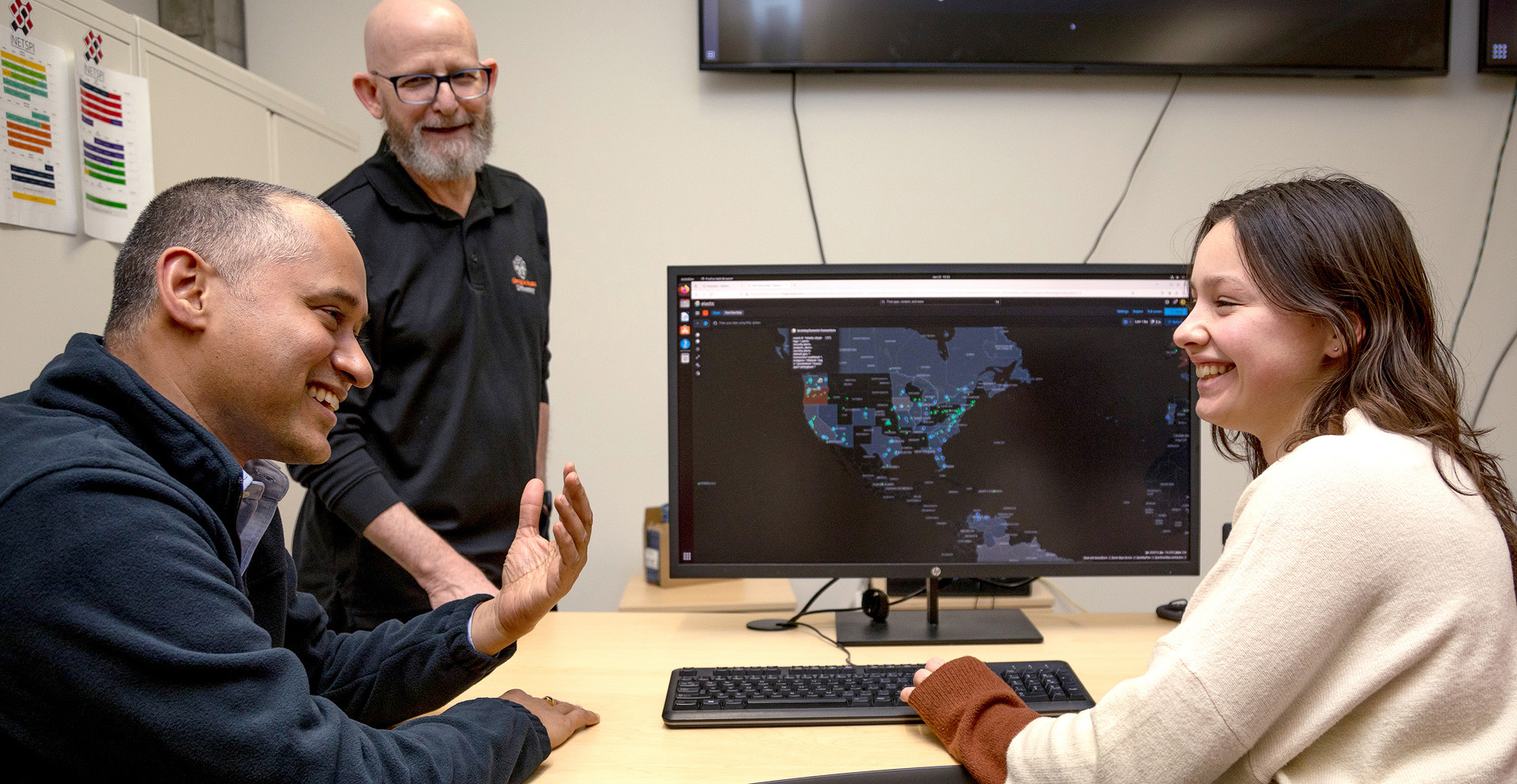 Two professors having a conversation with a student in front of a computer.