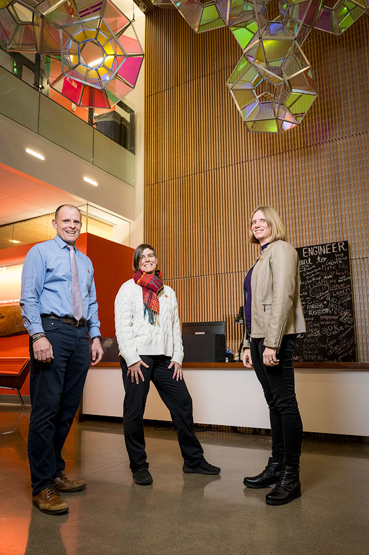 Three people stand beneath a glass sculpture in a lobby and face the camera.