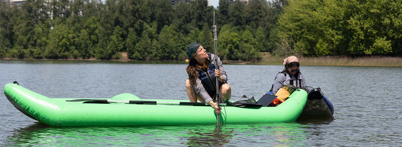 A person on a river in an inflatable kayak examines equipment in the water.