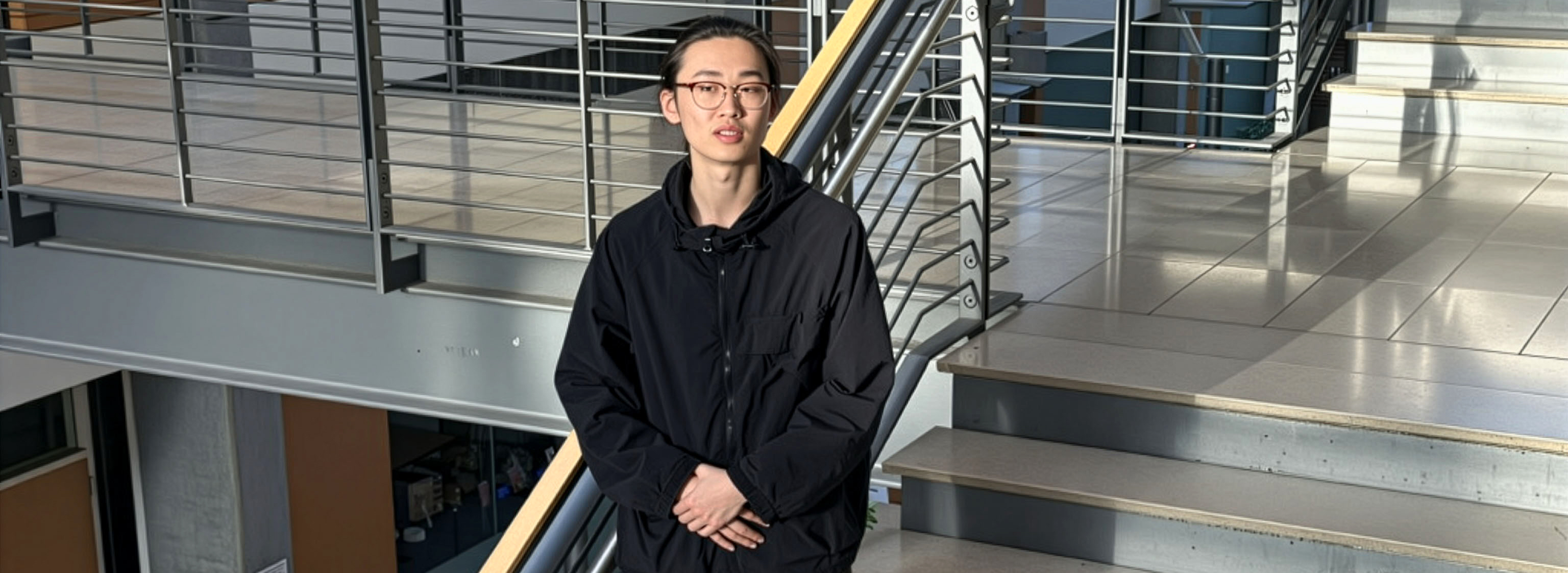 A person stands on stairs inside a contemporary office building with natural light shining on them. 