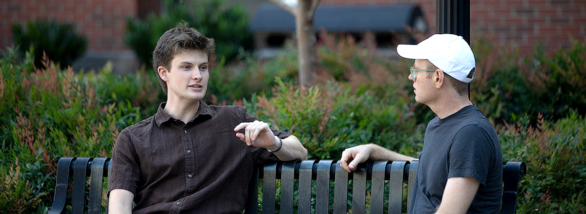 Two men sitting on a chair outside.