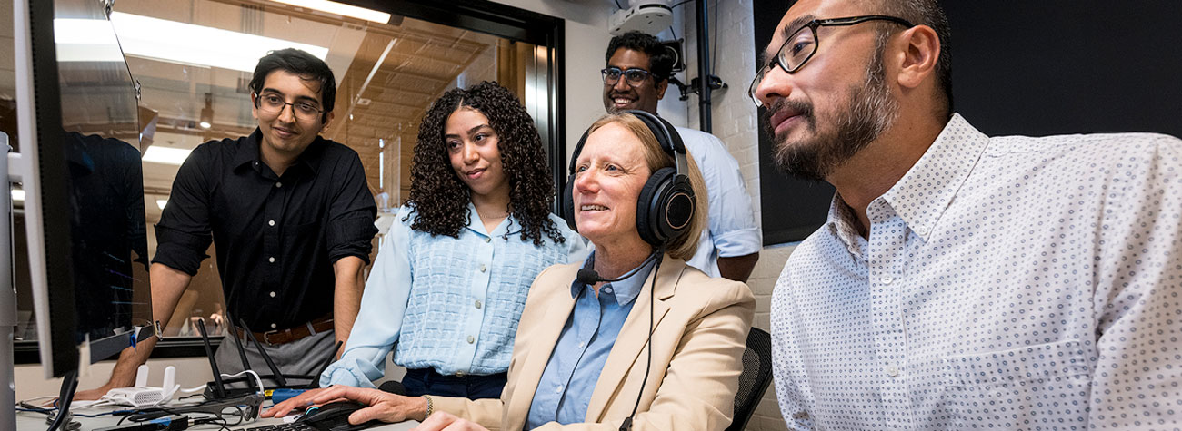 A professor and a group of students looking at a computer screen.