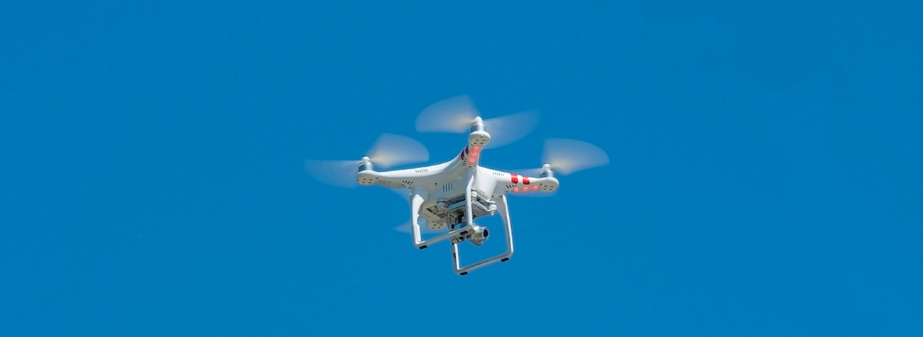 A drone hovers in the air against a clear blue sky.