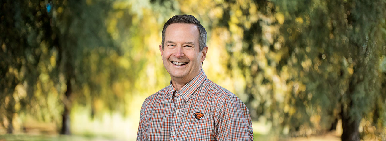 Smiling man wearing checkered shirted emblazoned with the Oregon State University beaver logo.