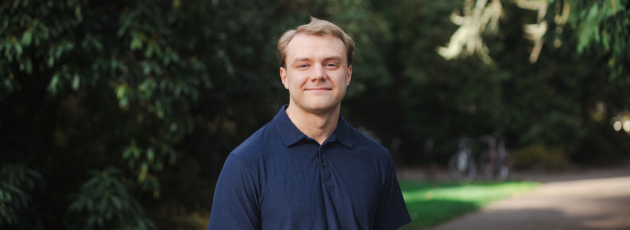 Maxwell Kavanaugh posing on a paved path with green grass and trees.