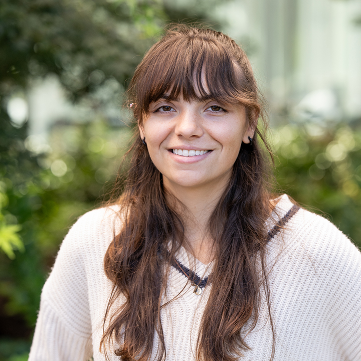 Emma Anderson stands outside in the sun with green vegetation.