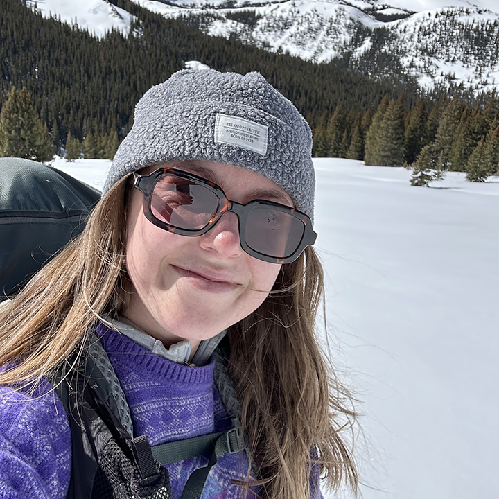 Jasmine Summers-Evans stands outside in the snow with mountains in the distance and looks toward the camera.