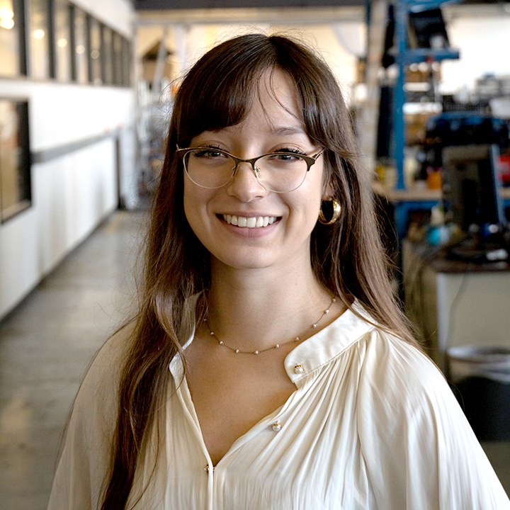 Loni Halsted-Ruelas stands in a lab environment with equipment behind them and smiles toward the camera.