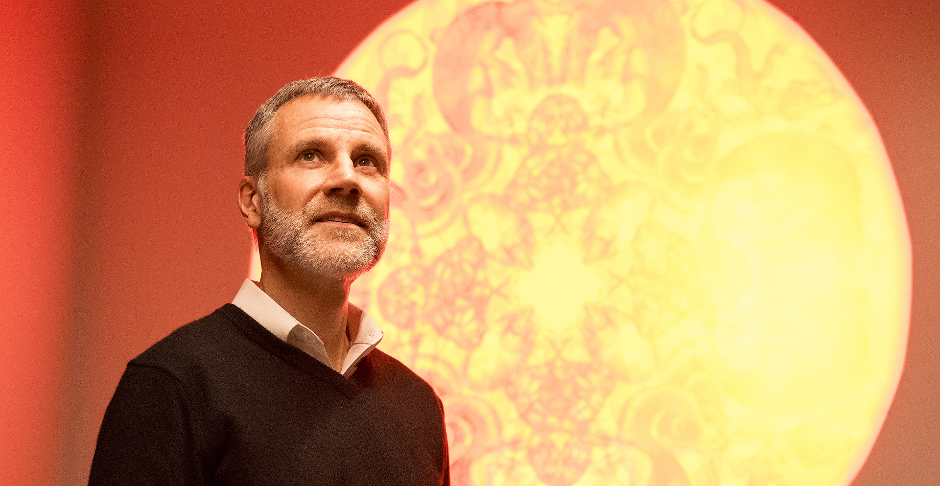 Dr Kevin Houser infront of a orange background showing lighting pattern