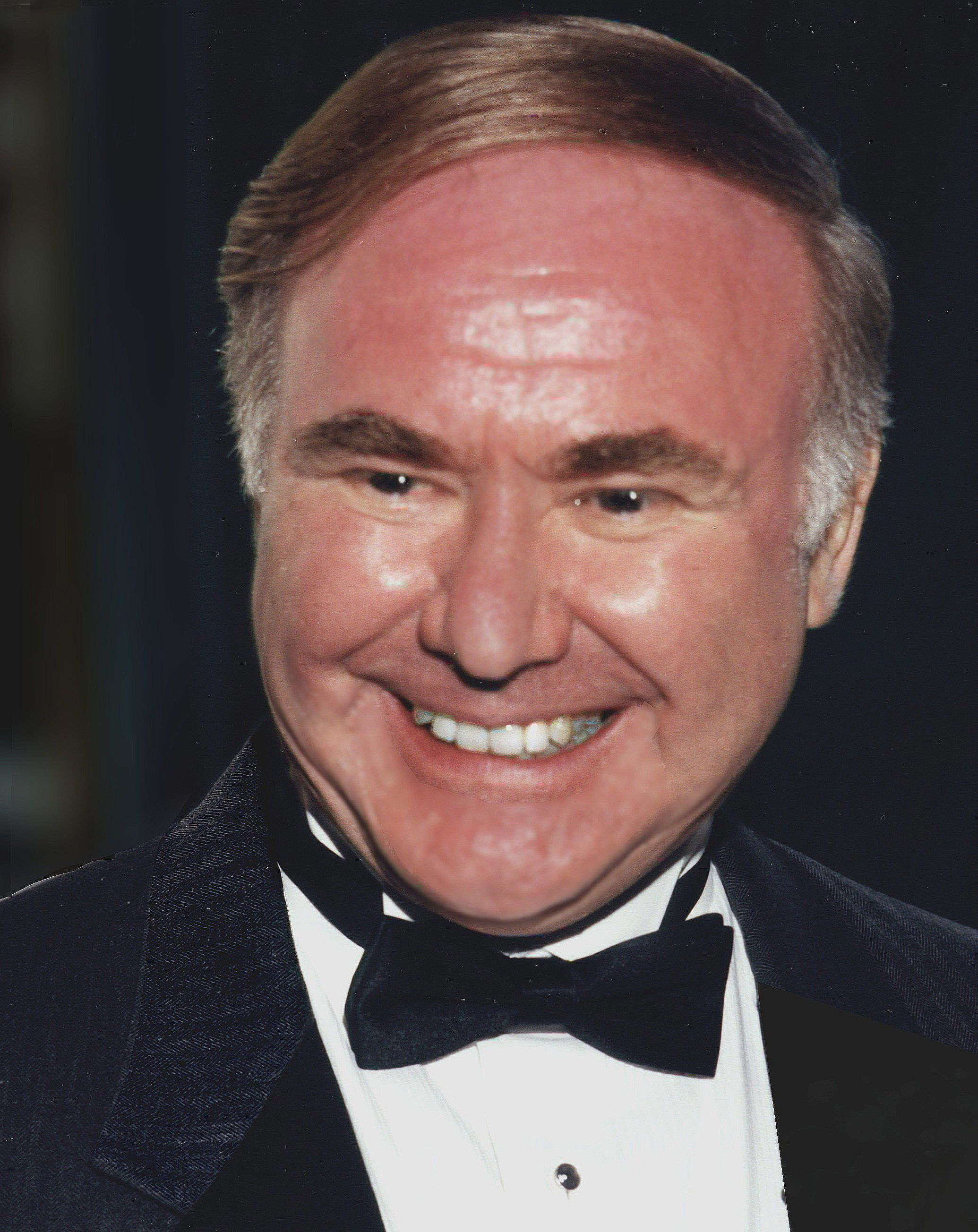 Barrie Gilbert wears a black tuxedo and bow tie and smiles with a dark background behind.