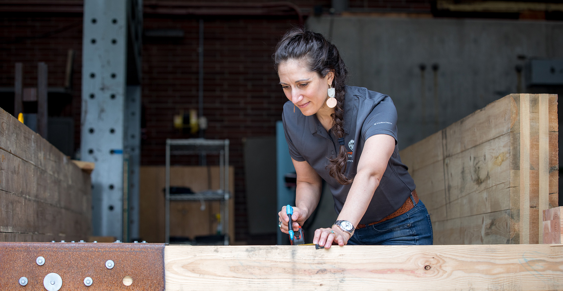 A female faculty member marking a piece of wood for measurement.