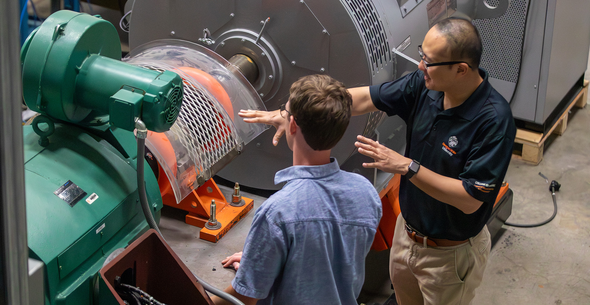 A professor talking to a student pointing towards a big machine.
