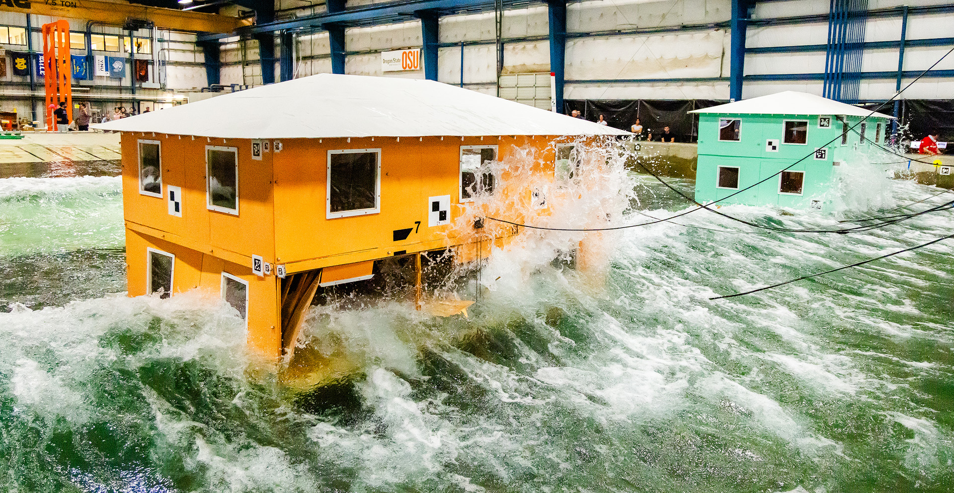 Huge artificial waves of water flowing in a lab environment with two small houses.