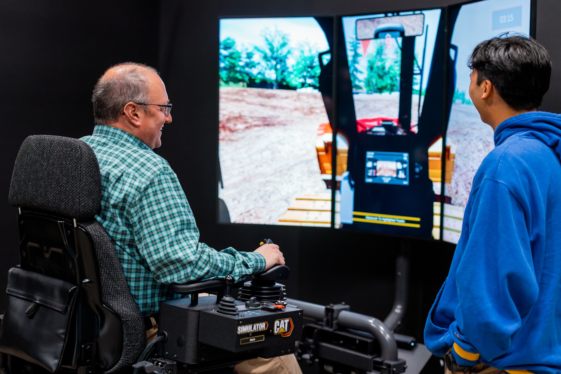 Researcher operating construction vehicle simulation while a student observes.