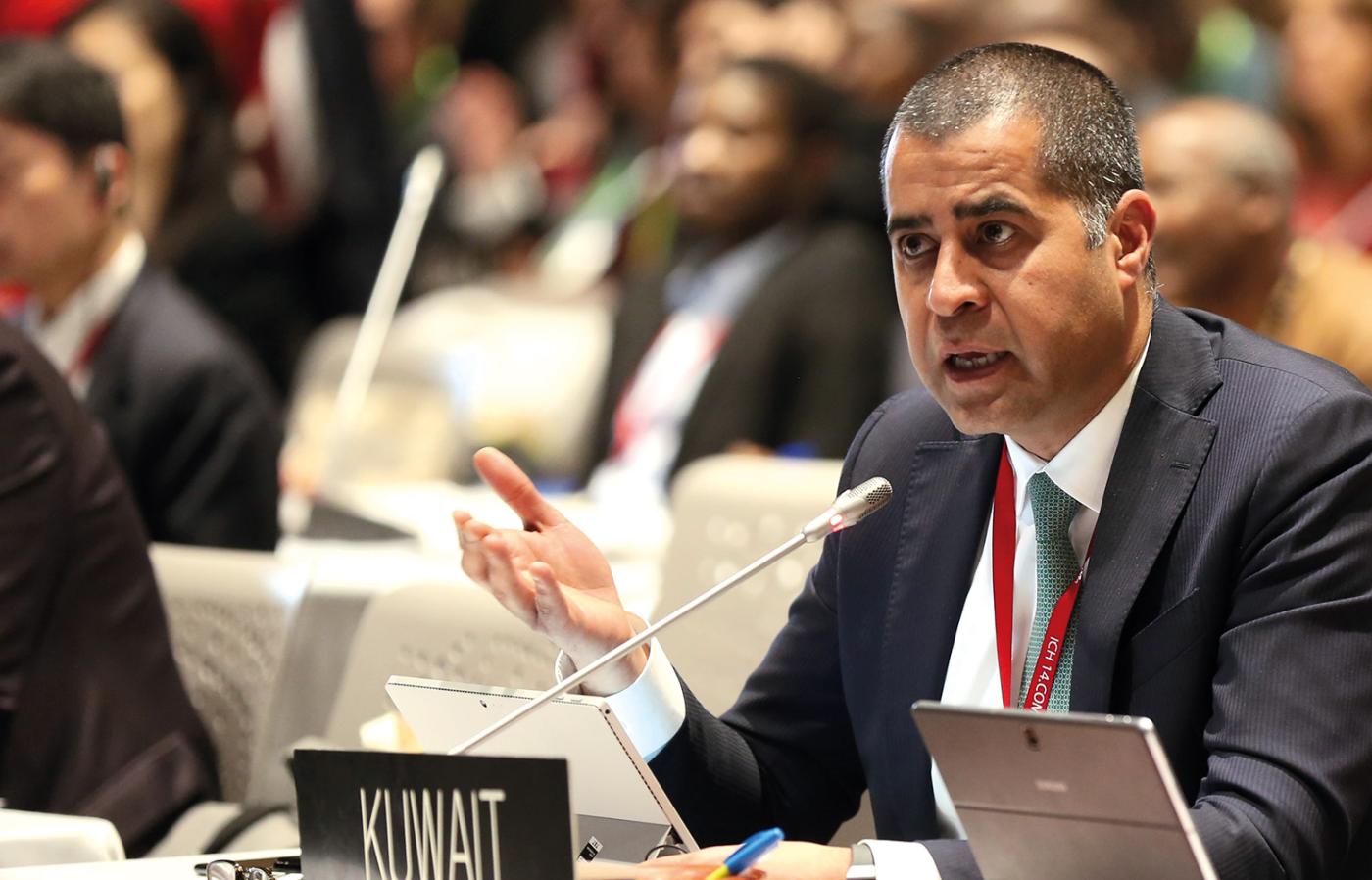 Ambassador Adam Al Mulla speaking into a small microphone at a conference. 