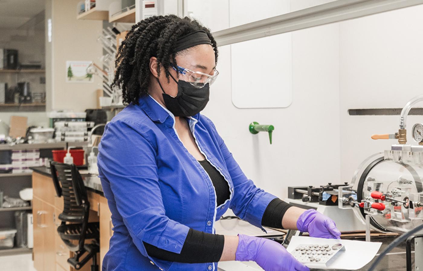 Kenya Hazell works at a lab bench, wearing gloves while handling small samples.