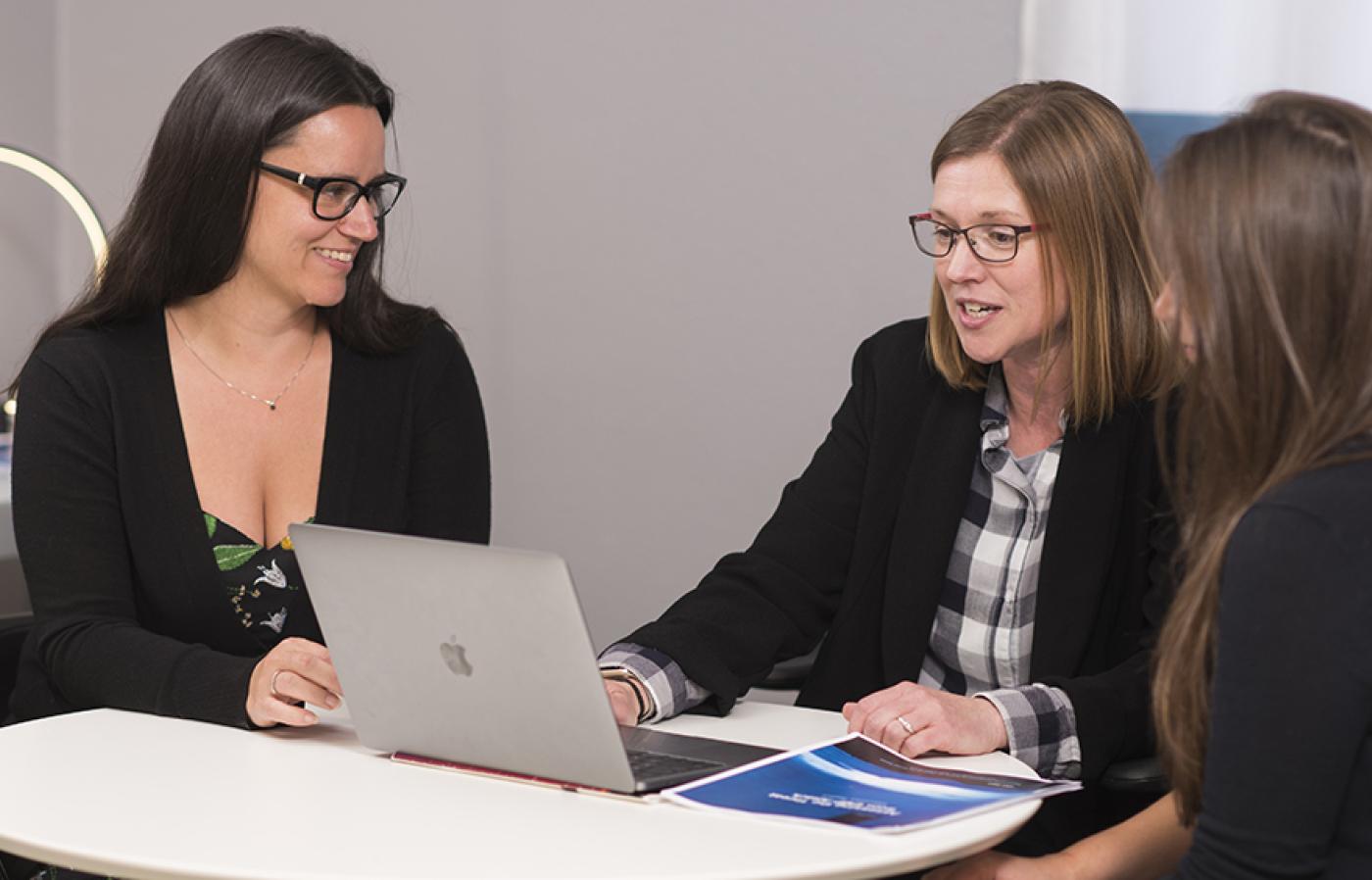 Charlotte Rose working on a laptop with Professor Camille Palmer and fellow grad student Ari Foley.