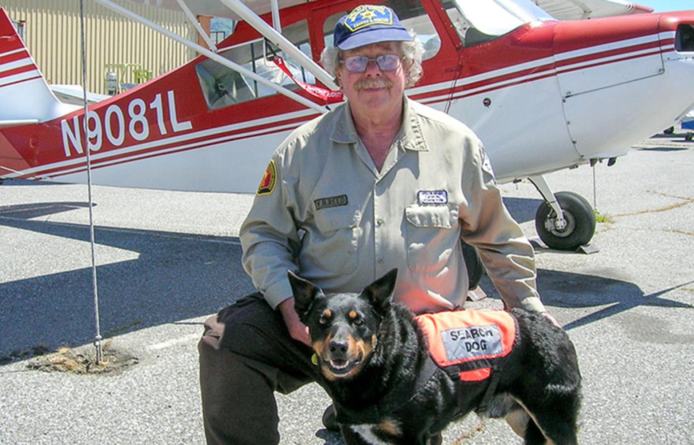 Bill Reed and his dog Scout posing in front of a small aircraft.