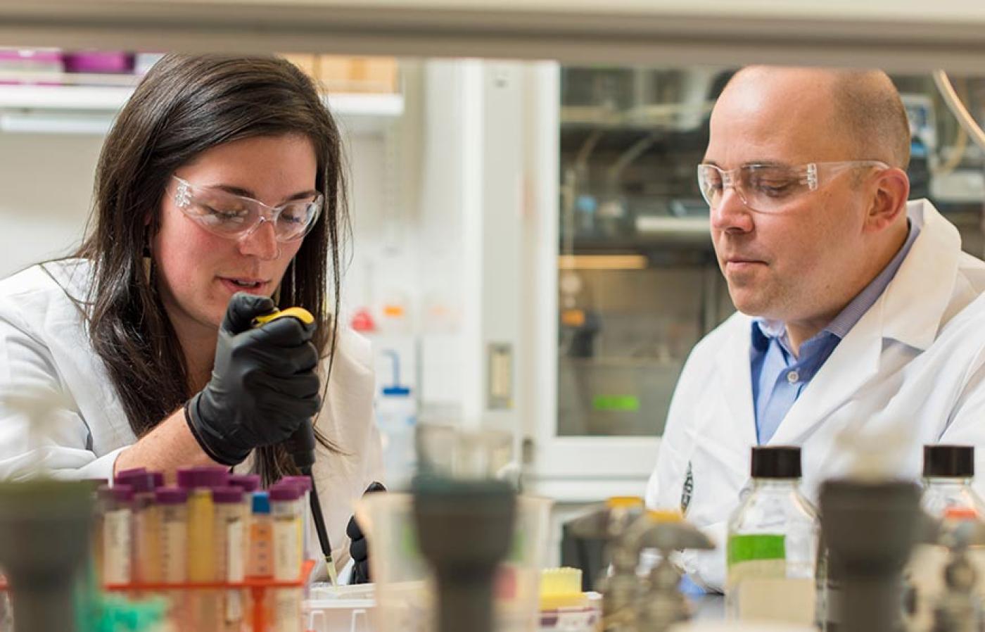 Two researchers wearing lab attire while working on a experiment.