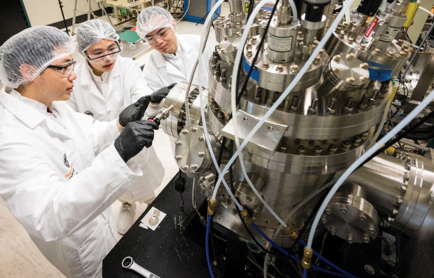Three students in lab uniform working on a machine.