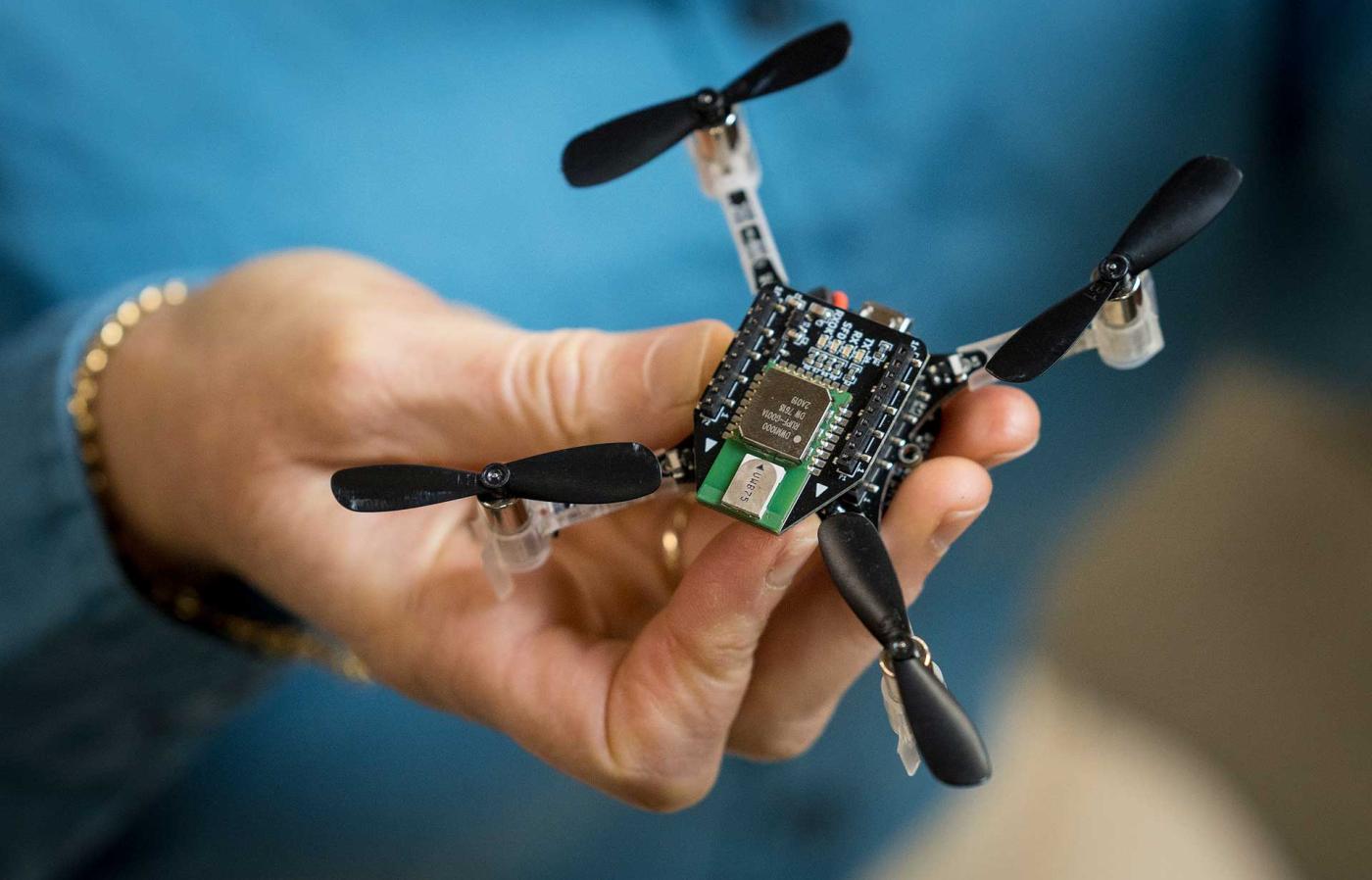 A hand holding a small drone with four propellers.