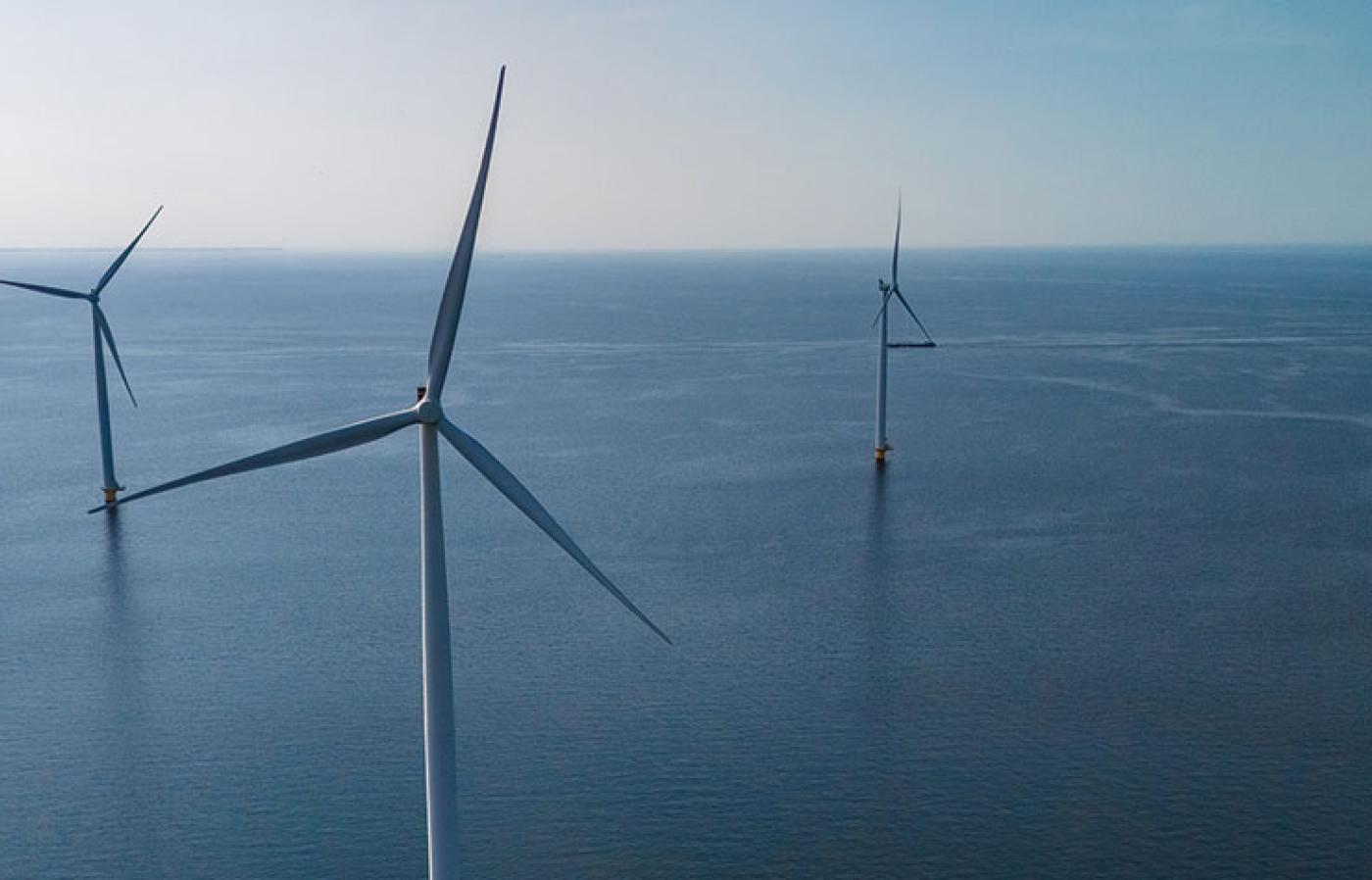 Four wind turbines in the ocean with the horizon in the distance. 