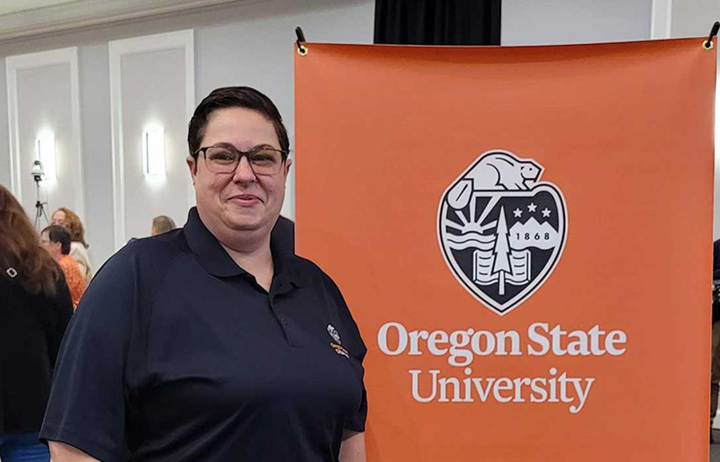 A person standing in front of an Oregon State University College of Engineering banner at an indoor event with others talking in the background.