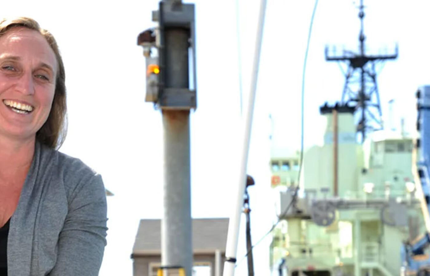 A person sitting outside looking at the camera with marine research equipment in the background.