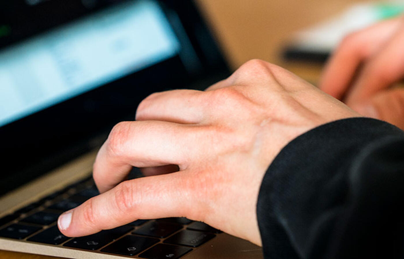 A person typing on a keyboard with a blurred digital screen in the background.