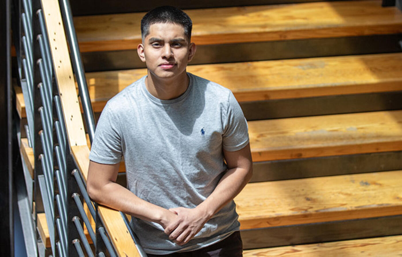 A person stands on wooden stairs within a large atrium and looks up at the camera.