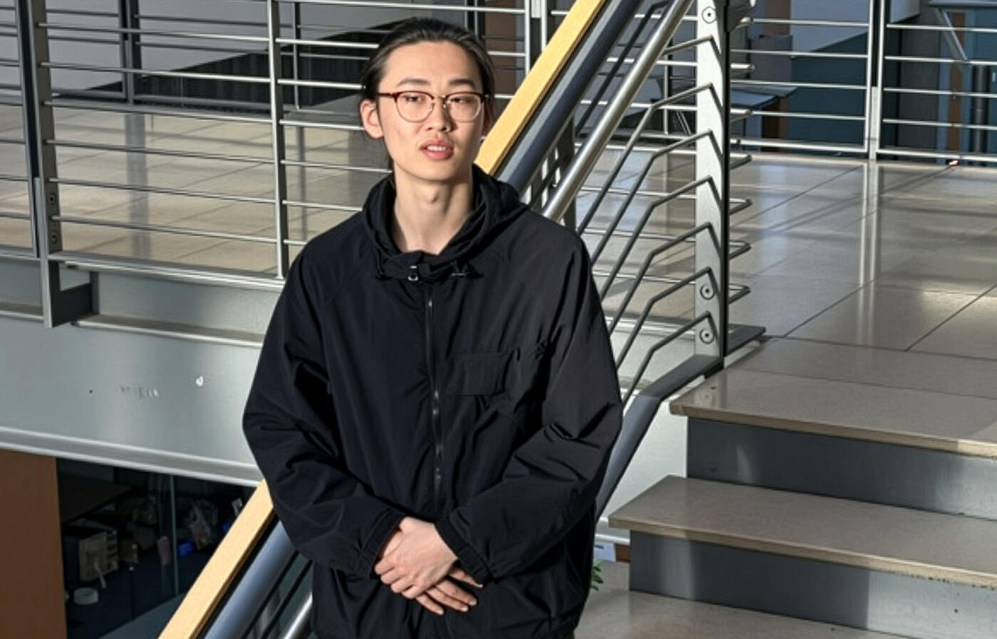 A person stands on stairs inside a contemporary office building with natural light shining on them. 