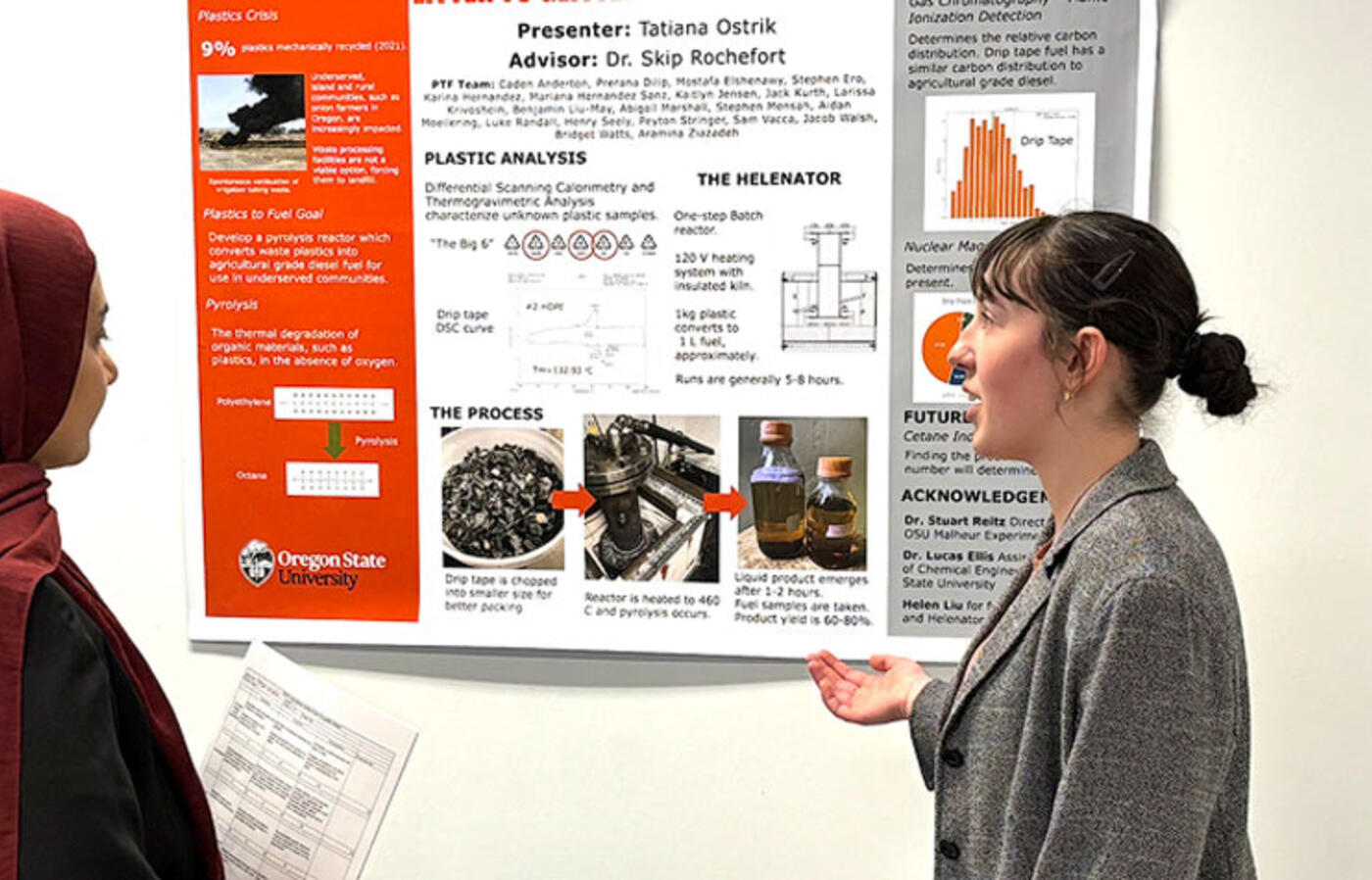 A woman presents a poster to a fellow student during a tabling event.