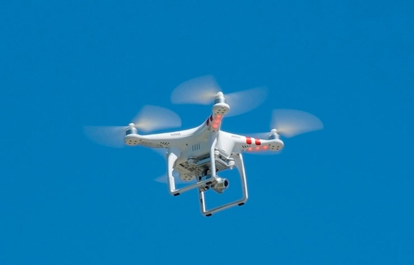 A drone hovers in the air against a clear blue sky.